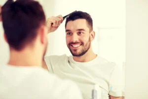 Ein junger Mann, der nach einer Haartransplantation sein Haar vor dem Spiegel kämmt.